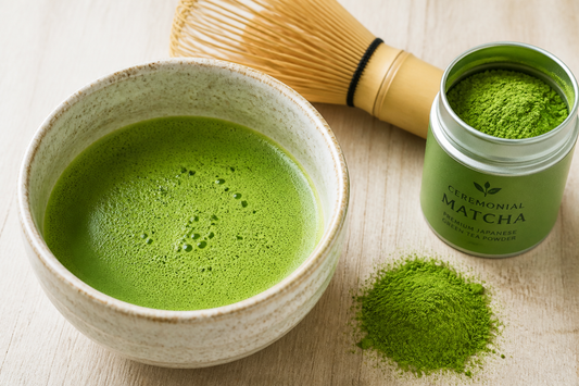 A bowl of bright green matcha with a bamboo whisk and matcha powder on a wooden surface.